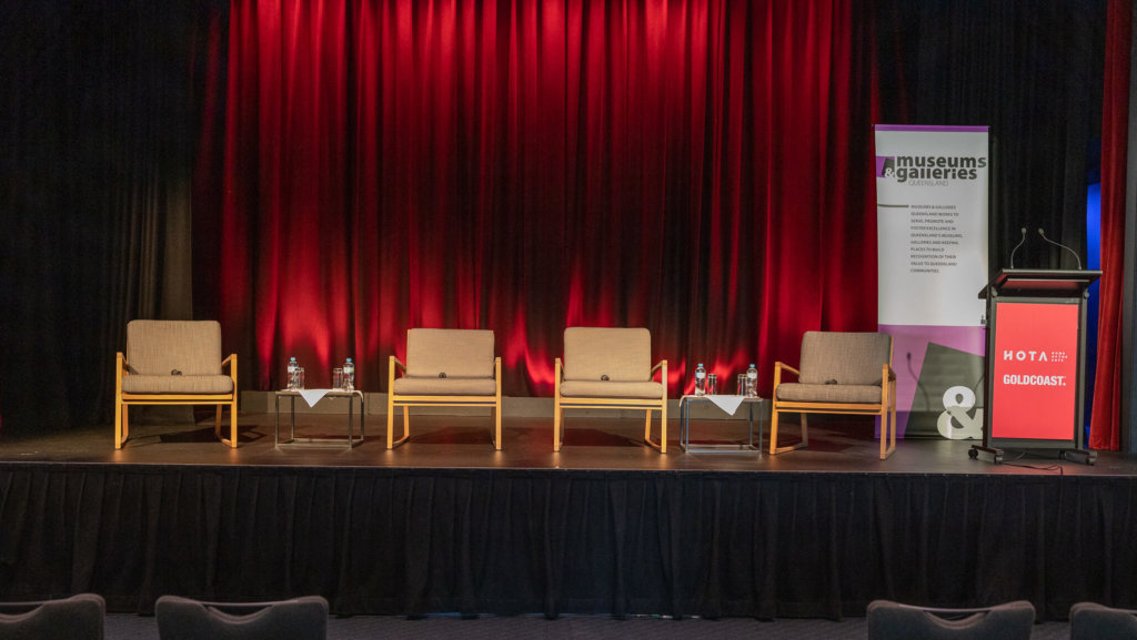 Empty chairs on a stage with M&G QLD banner